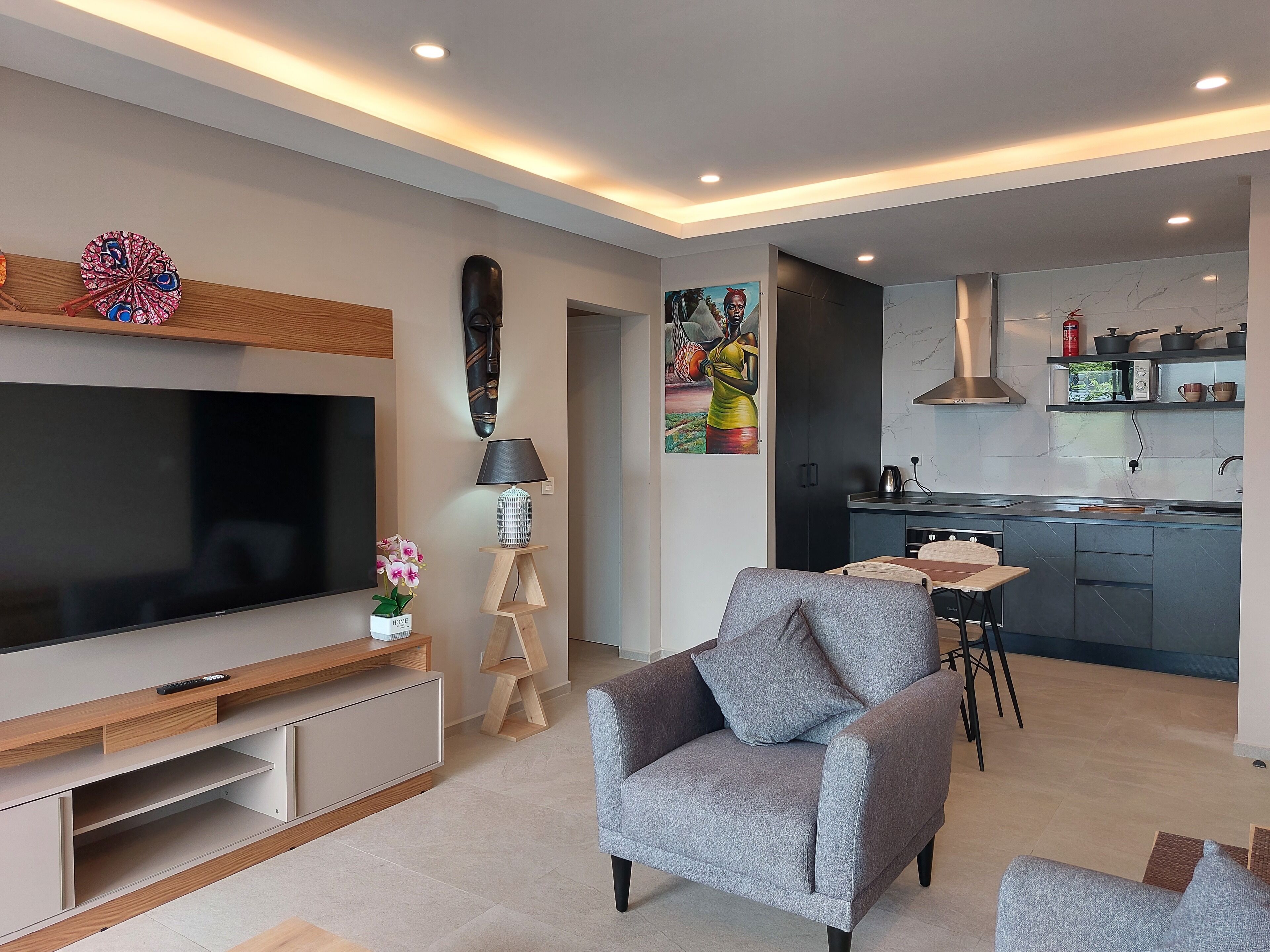 A modern living room with a flat-screen TV, grey armchair, and a small dining area.