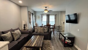 A modern living room with a sectional sofa, a coffee table, and a TV mounted on the wall. - Two Bedroom Basement Apartment (Conyers)