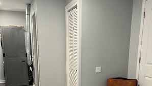 A hallway with grey walls, a wooden floor, a white door, and a brown bench. - Two Bedroom Basement Apartment (Conyers)