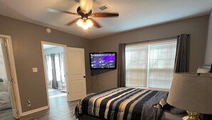 A bedroom with a bed, a ceiling fan, a TV, and a window with curtains. - Two Bedroom Basement Apartment (Conyers)