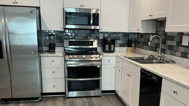 A modern kitchen with white cabinets, stainless steel appliances, and a grey tiled backsplash. - Two Bedroom Basement Apartment (Conyers)