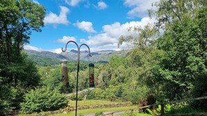 Un espacio al aire libre con vistas, una cerca de madera, un camino de piedra y un comedero para pájaros de metal.