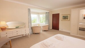 Habitación de hotel con cama, tocador con espejo, una silla, ventana con cortinas y armario.