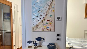 A bedroom with a bed, a dresser with decorative items, and a painting of a beach scene. - HOUSE OLEANDRI 200m from the beach (PUNTA ALA)