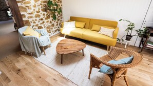 A cozy living room with a yellow sofa, a wicker chair, a wooden coffee table, and a stone wall.