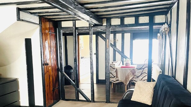 A room with a wooden floor, a sofa, a table, and a chair. There is a door leading to another room. - Immaculate 3-bed House in Waltham Cross (Waltham Cross)