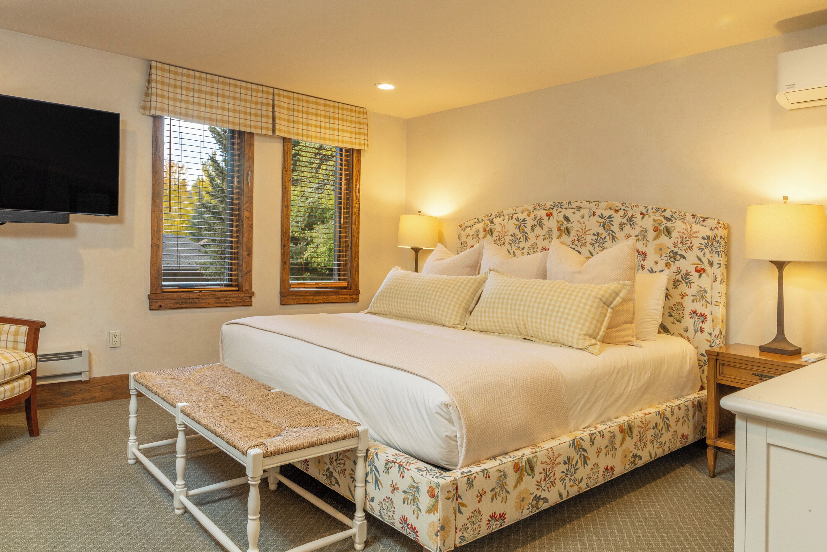 A bedroom with a large bed, a bench, a television, and two lamps.