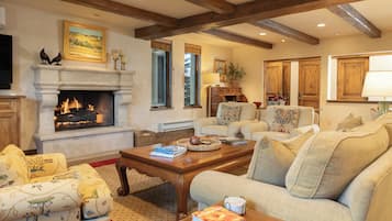 A cozy living room with a fireplace, comfortable seating, and wooden beams on the ceiling.