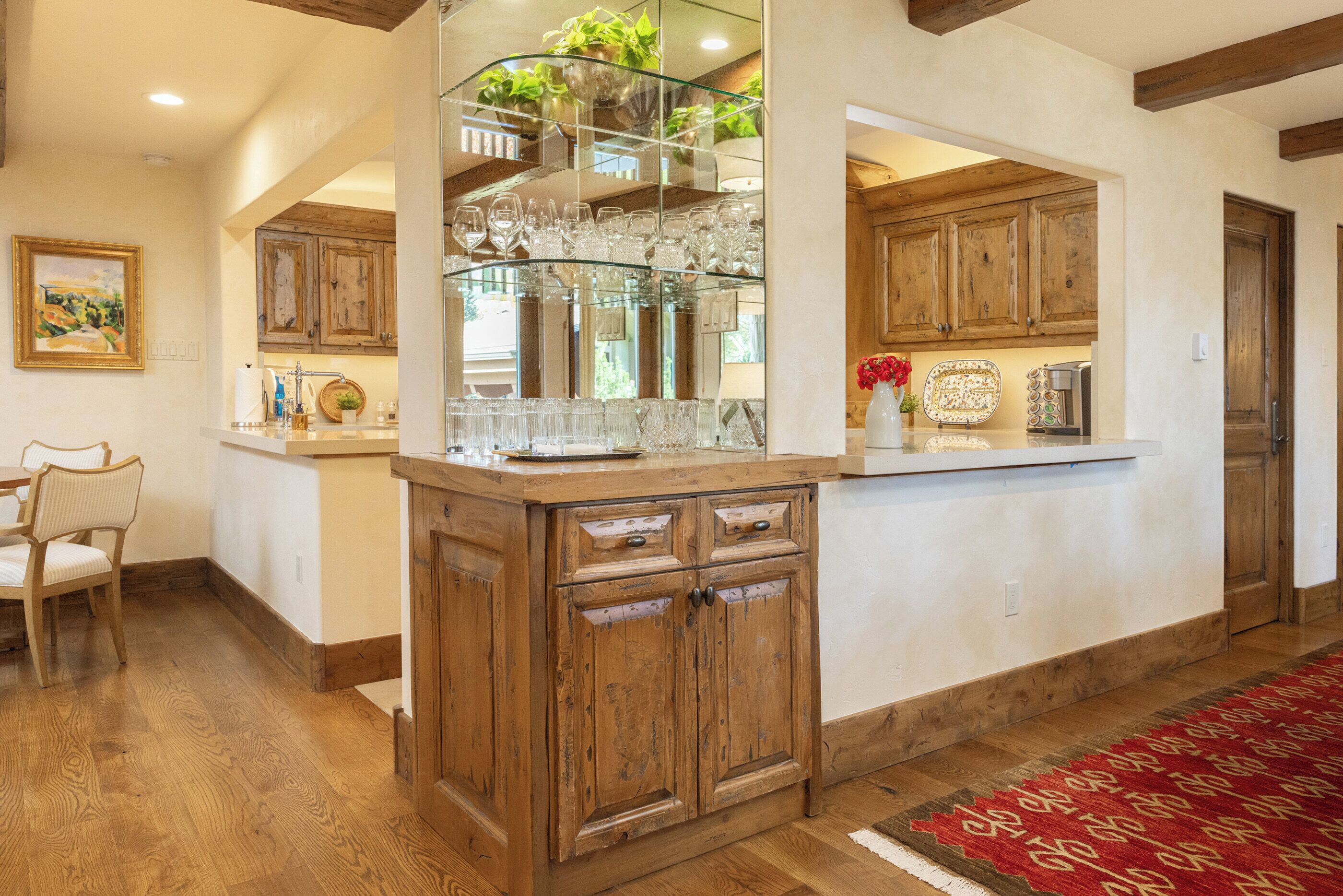 A kitchen with wooden cabinets, a glass display shelf, and a red patterned rug.