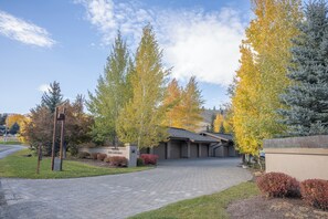 Ein Wohnweg führt zu einem Haus mit Garage, umgeben von Bäumen im Herbstlaub, und ein klarer Himmel.