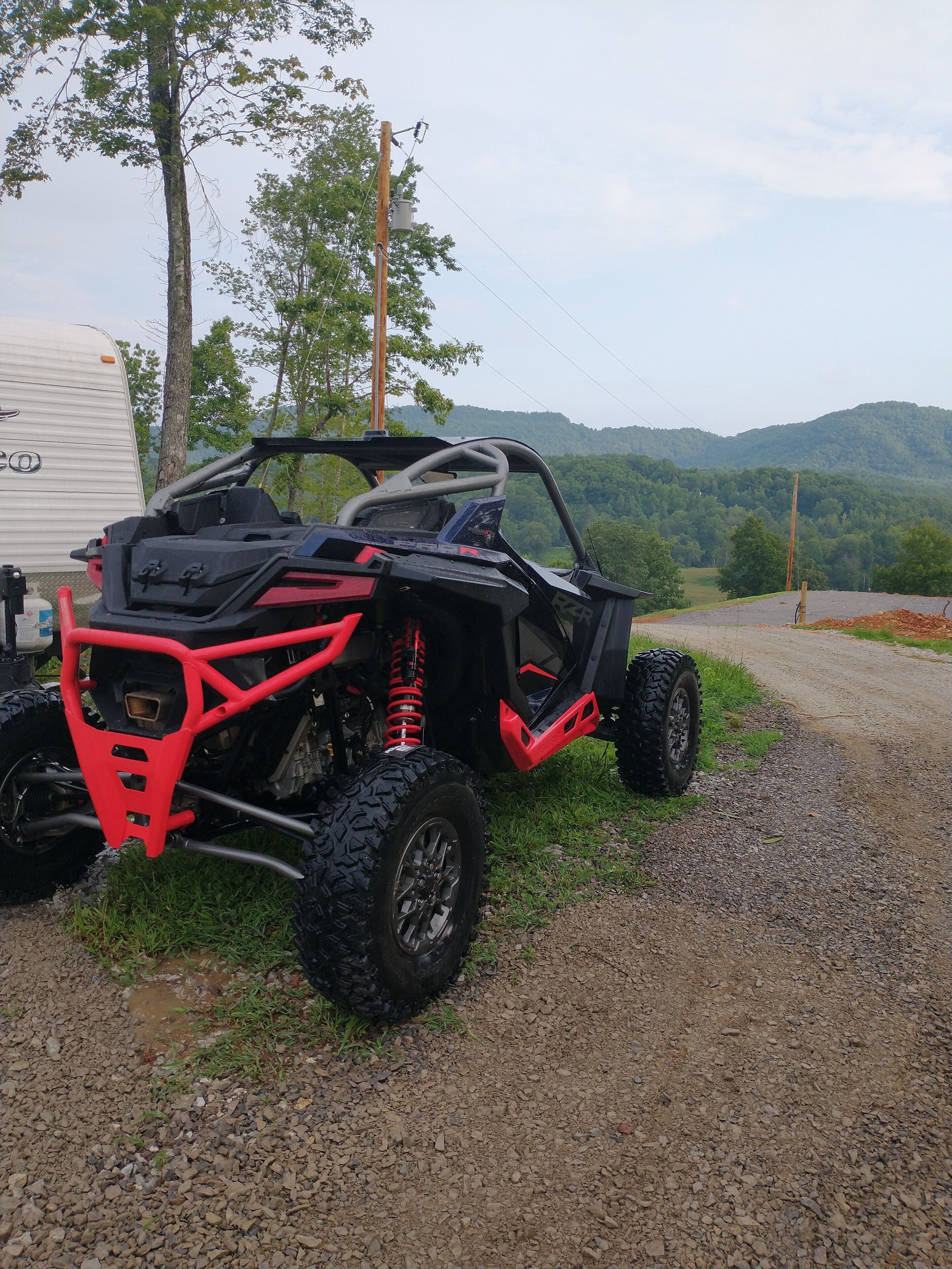 A red and black ATV parked on a gravel path with a trailer in the background and a mountainous landscape.