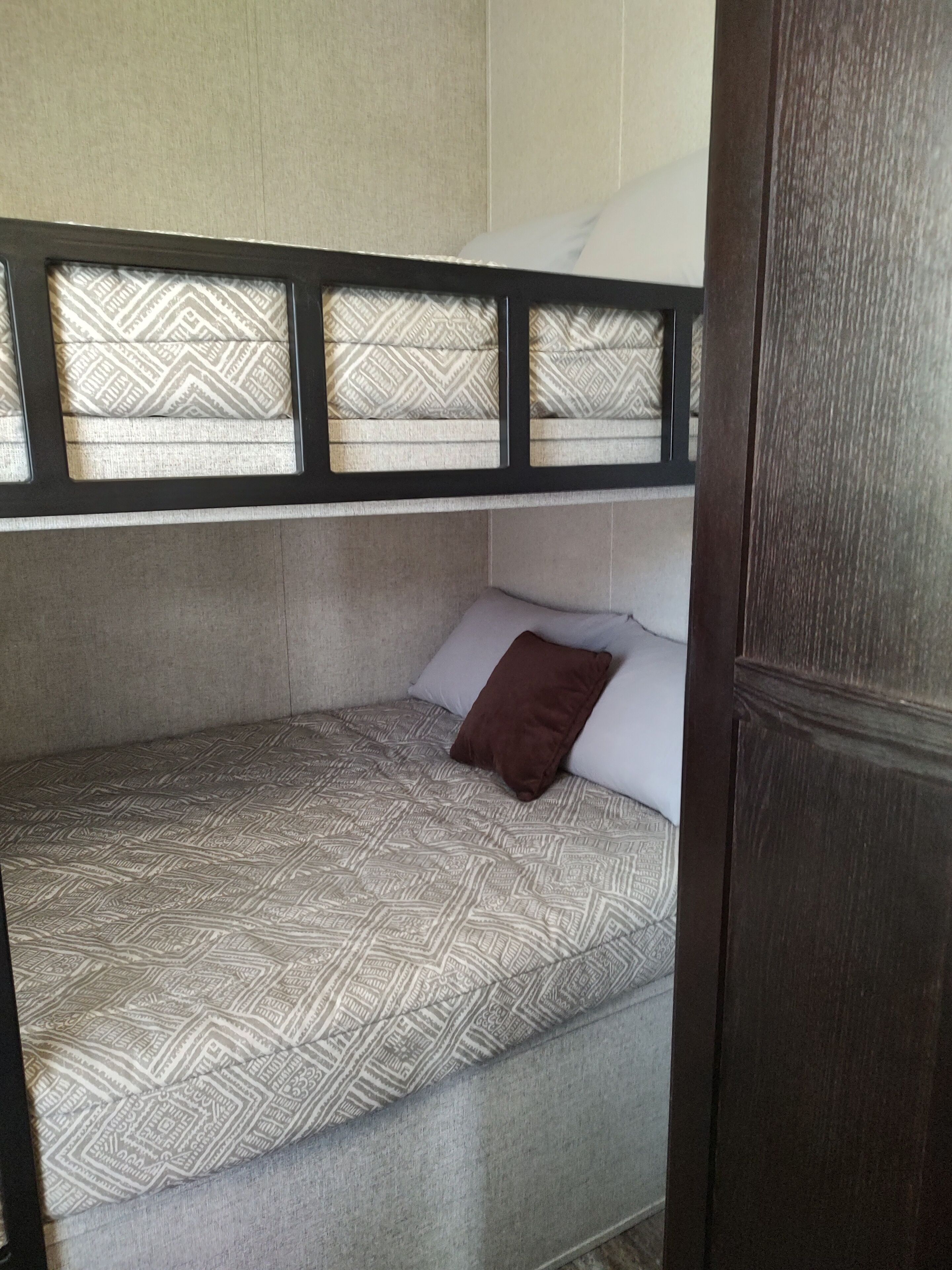 A bunk bed with patterned bedding, a brown pillow, and a wooden headboard.