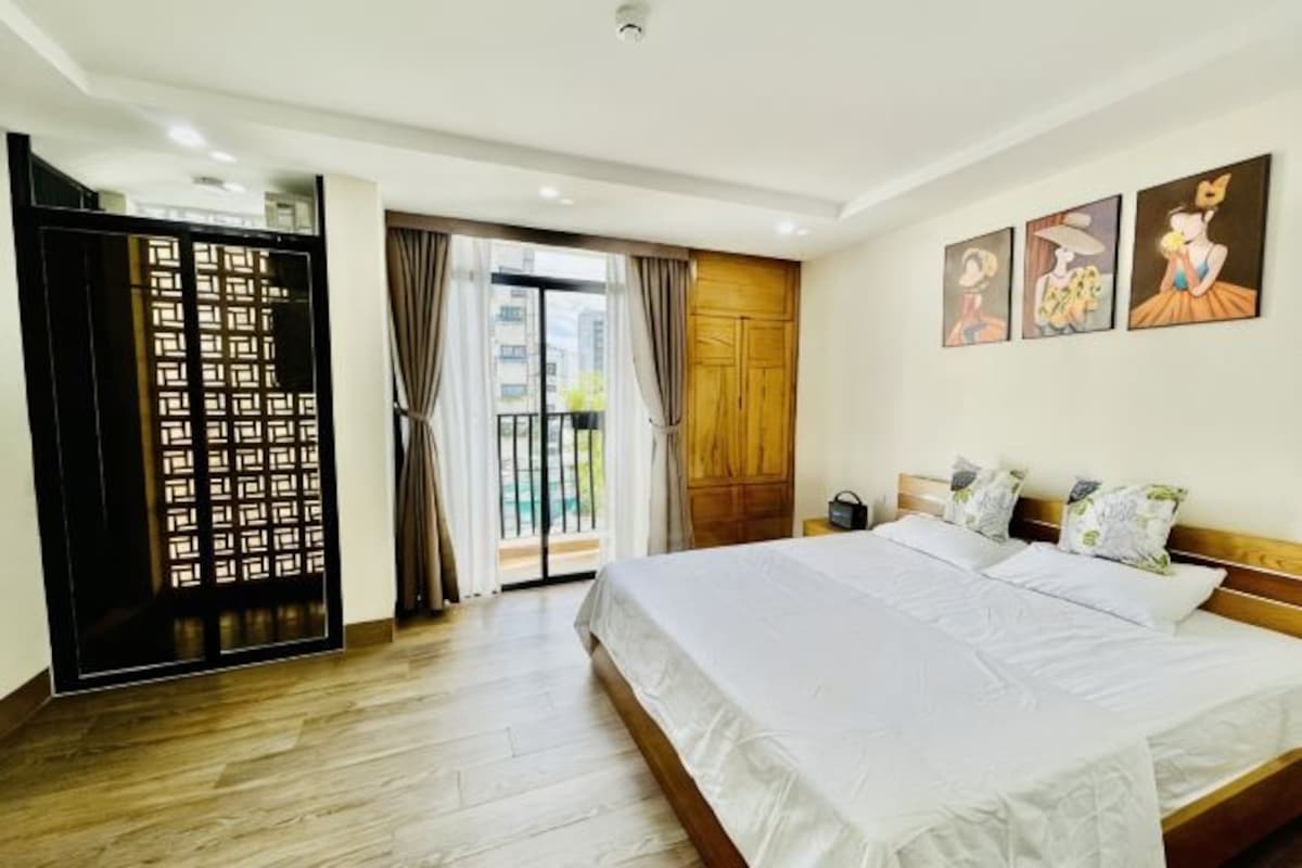 A hotel room with a large bed, a sliding door, and a balcony with curtains.