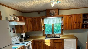 Una cocina con armarios de madera, estufa, lavamanos y ventana con vista a zonas verdes.