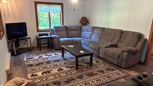 Una sala de estar con un sofá modular, una mesa de centro, un televisor y un ventilador de techo.