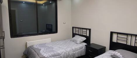 A bedroom with two beds, a window, and a ceiling light.