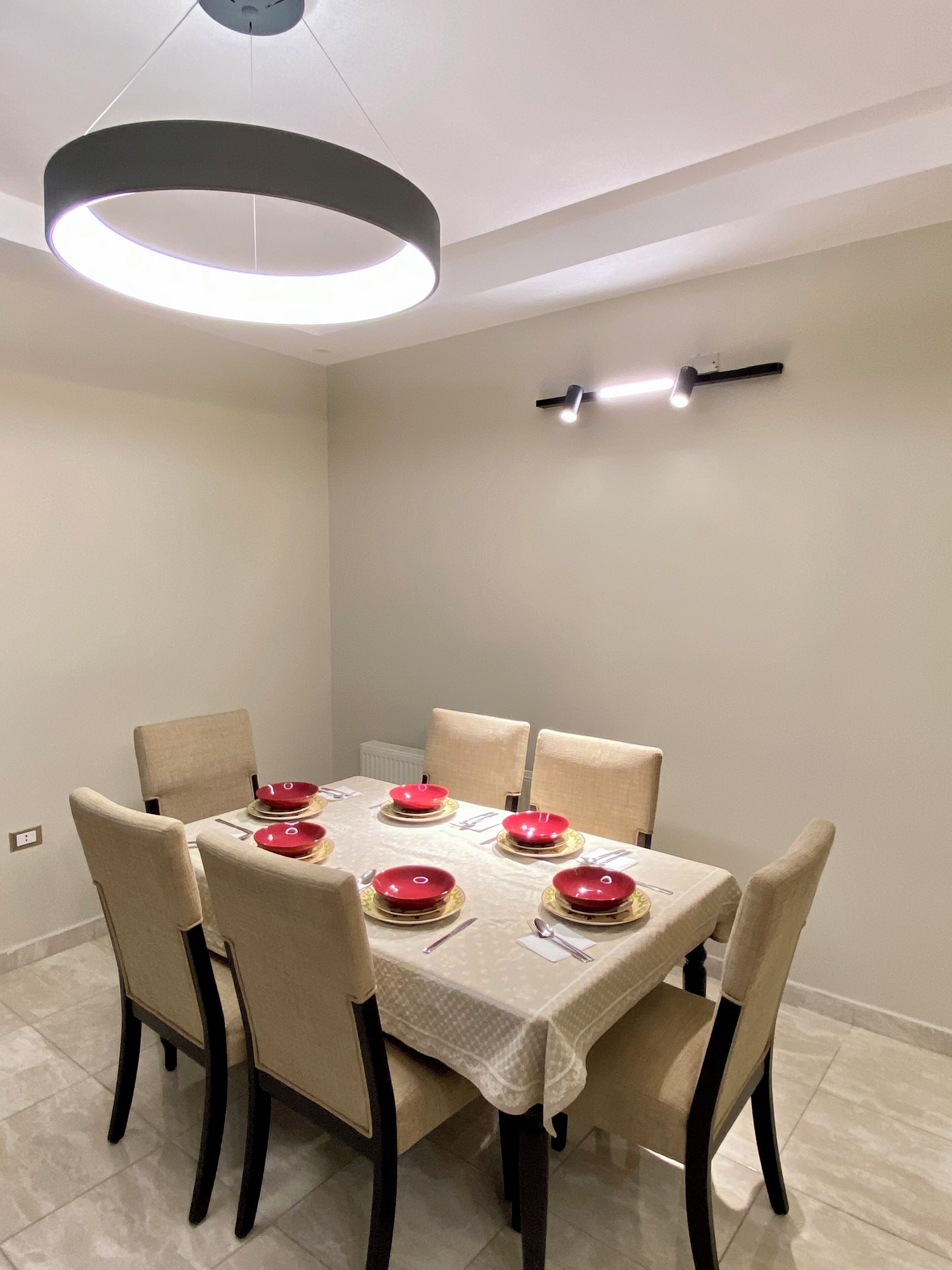 A dining area with a round table set for six, six chairs, and a modern pendant light fixture above.