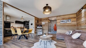 A modern living room with a wooden floor, a brown sofa, a dining area with yellow chairs, and a kitchen with dark cabinets. - Very nice apartment, 3 Bedrooms Very nice view (Val-d'Isère)