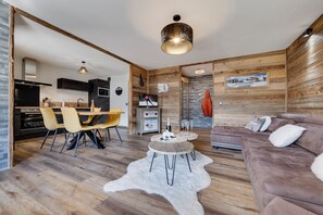 Una sala moderna con suelo de madera, un sofá marrón, una zona de comedor con sillas amarillas y una cocina con armarios oscuros.