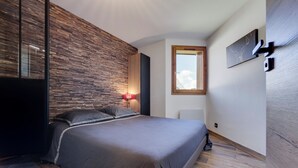 A modern bedroom with a large bed, a wooden accent wall, a nightstand, and a wall-mounted TV. - Very nice apartment, 3 Bedrooms Very nice view (Val-d'Isère)