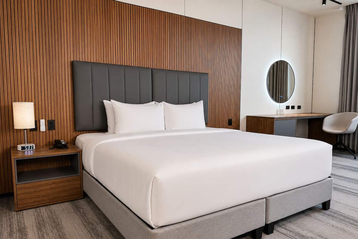A hotel room with a large bed, a bedside table with a lamp, a desk, and a chair.