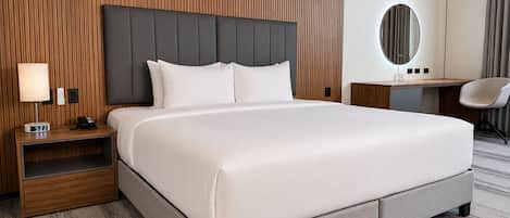 Una habitación de hotel con una cama grande, una mesita de noche con lámpara, un escritorio y una silla.