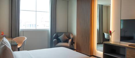 Una habitación de hotel con una cama grande, una silla, un escritorio con televisor y una ventana con cortinas.
