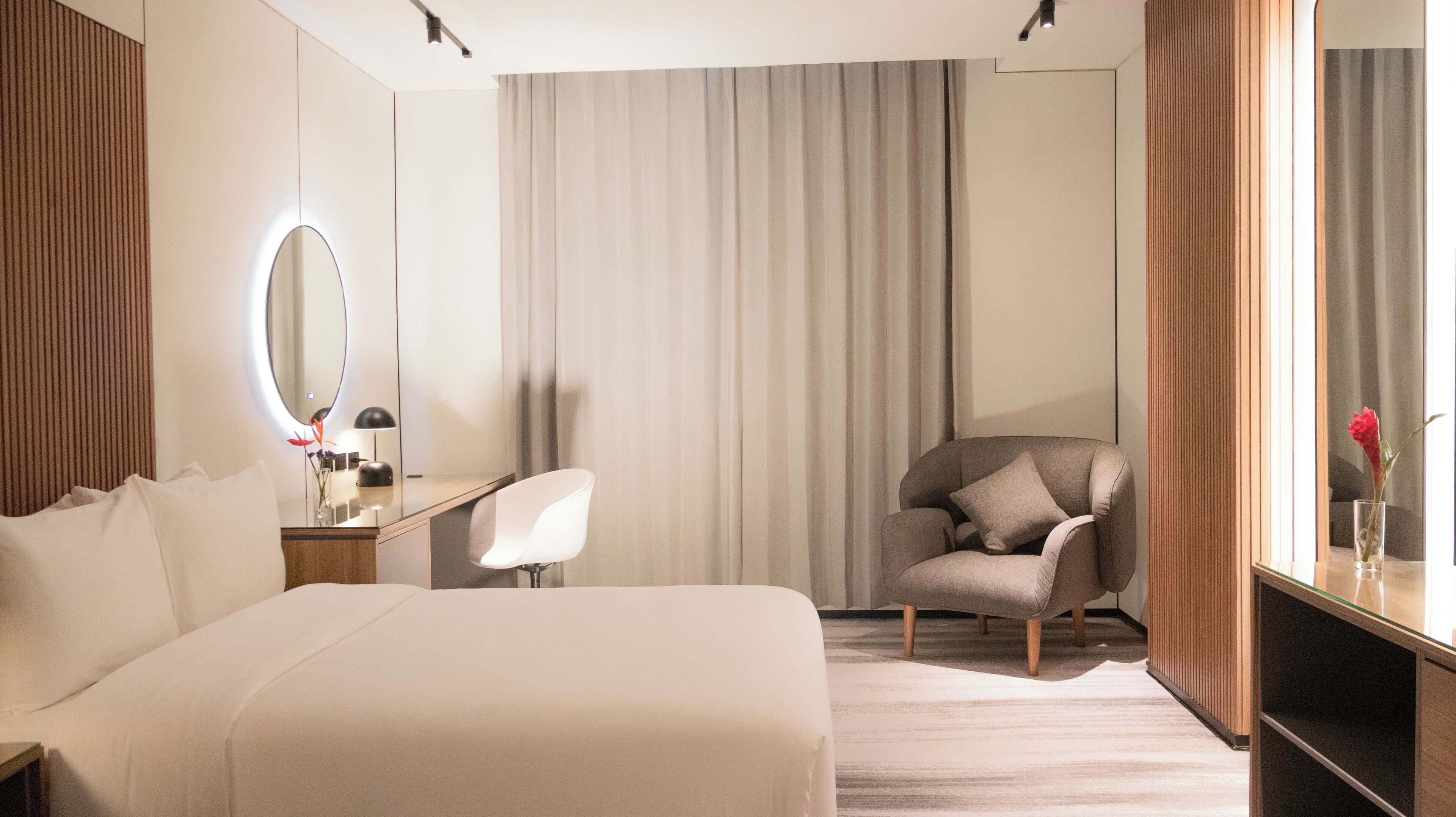 Habitación de hotel con cama, escritorio, silla, espejo y ventana con cortinas.