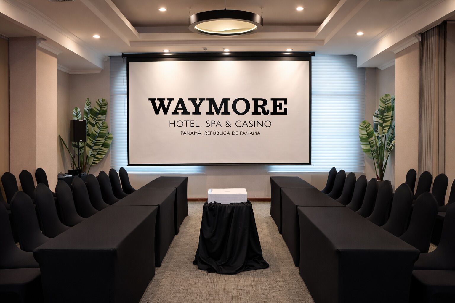 Ein Konferenzraum mit einer großen Leinwand, die die Marke 'WAYMORE HOTEL, SPA & CASINO PANAMÁ, REPÚBLICA DE PANAMÁ' zeigt.