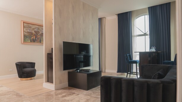 A modern living room with a flat-screen TV, a dark armchair, a sofa, and a dining area with a table and chairs. - Waymore Hotel Spa & Casino (Panama City)