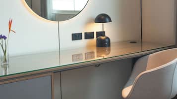 A modern bedroom with a glass desk, a round mirror, a lamp, and a chair.