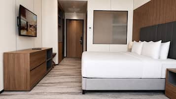 Una habitación de hotel moderna con una cama grande, un televisor montado en la pared, un aparador de madera y una puerta que da a un baño.