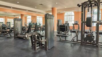 Un gimnasio con diversas máquinas de ejercicio, amplias ventanas y paredes anaranjadas.