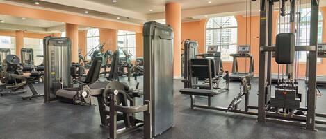 A gym with various exercise machines, large windows, and orange walls.