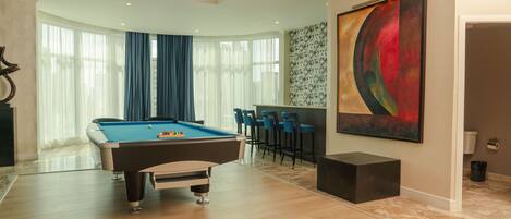 A pool table in a room with a large abstract painting, a dining area with chairs, and a modern ceiling design.