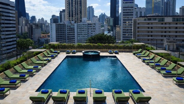 Piscina en la azotea con tumbonas y un horizonte urbano de fondo.