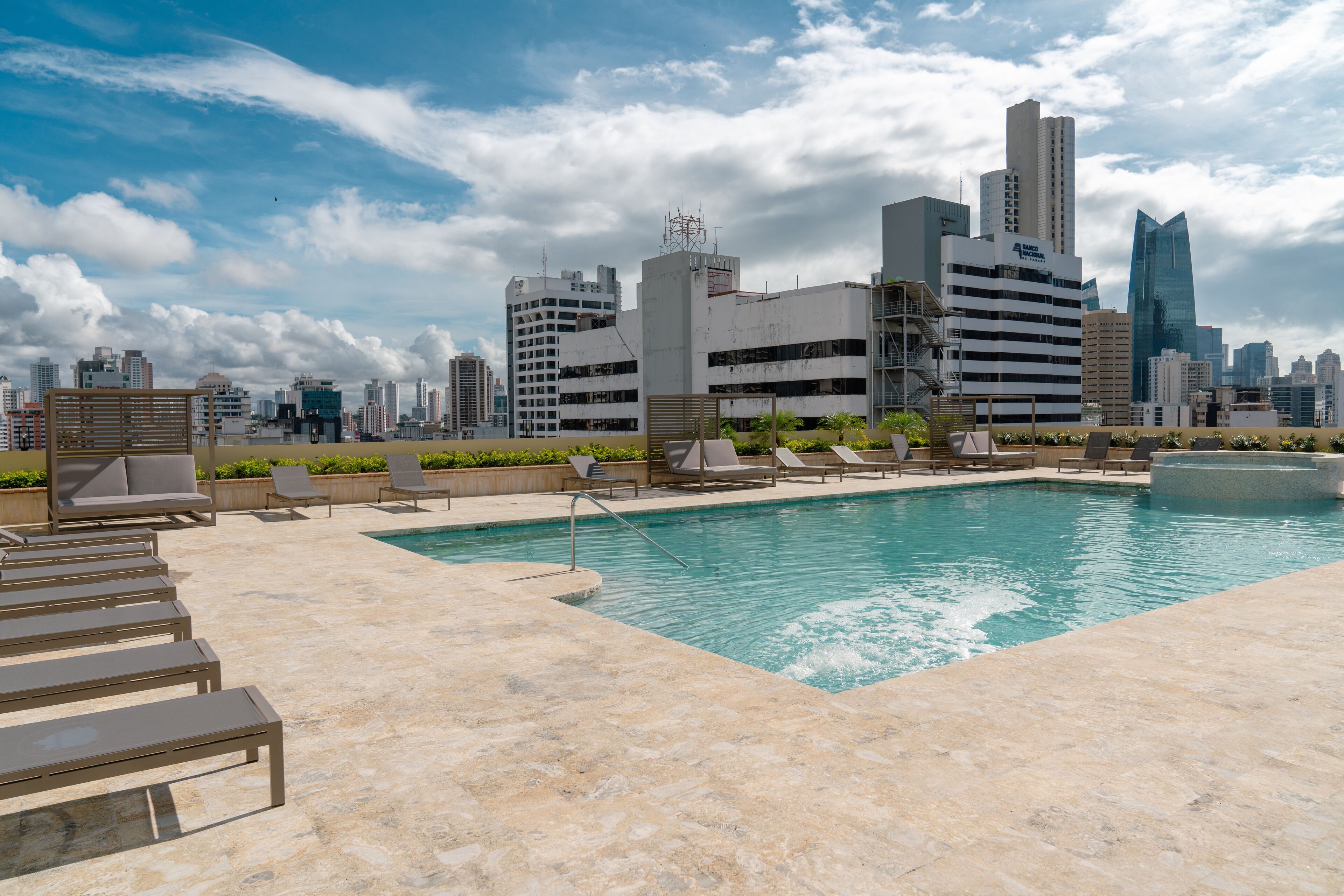 A rooftop pool with lounge chairs and a city skyline in the background.