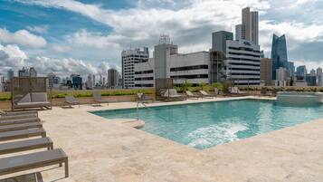 A rooftop pool with lounge chairs and a city skyline in the background.