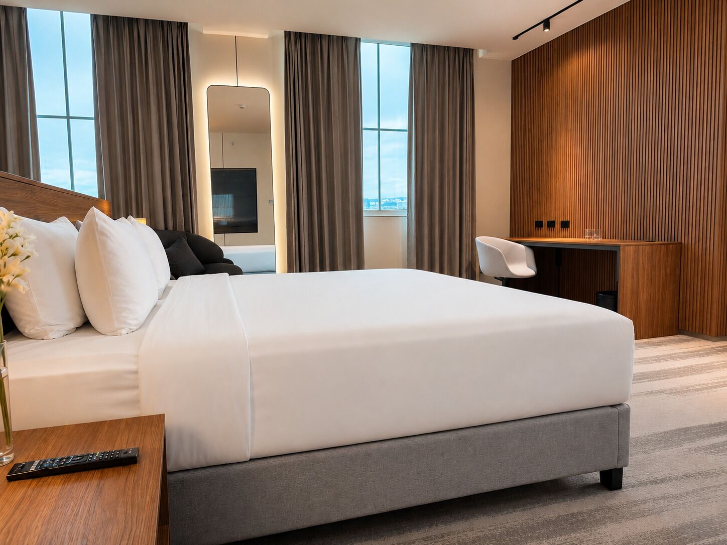 A modern hotel room with a large bed, a desk, and a view through the window.