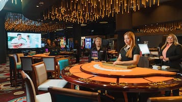 A casino with a blackjack table, chairs, and a large screen displaying a game.