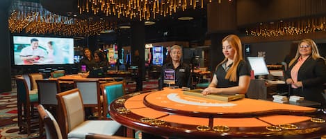 Un casino con una mesa de blackjack, sillas y una pantalla grande mostrando un juego.