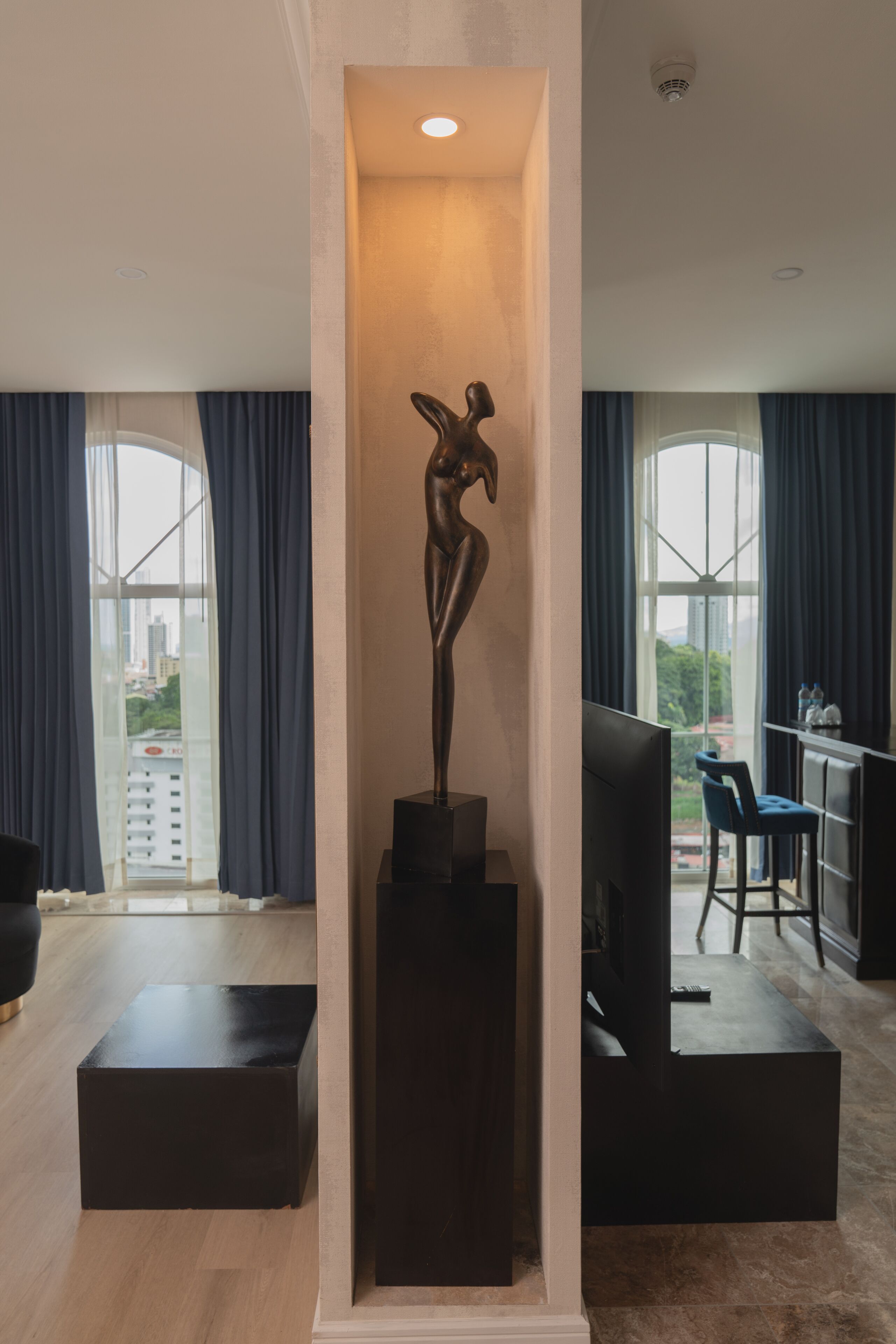 Una sala de estar moderna con una escultura sobre un pedestal, un televisor de pantalla plana y un comedor con barra.