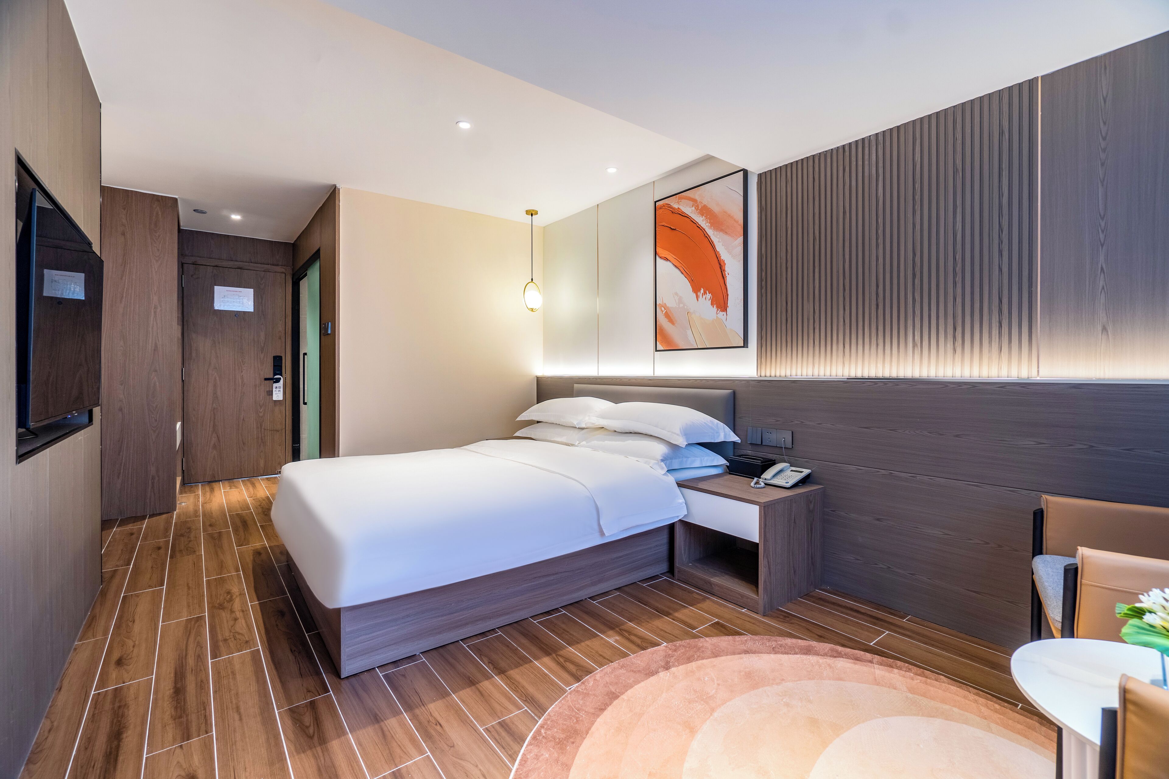 Quarto de hotel moderno com uma cama grande, mesa de cabeceira e pequena escrivaninha com cadeira.