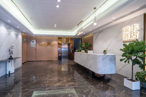 Un hall d’accueil d’hôtel avec un comptoir de réception en marbre, un mur en bois et un ascenseur moderne.