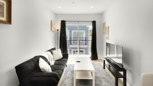 A modern living room with a black sofa, white coffee table, and a flat-screen TV. - Cozy Petworth Stay with Balcony & Courtyard View (Washington)