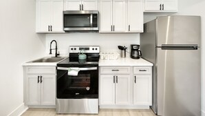 A modern kitchen with white cabinets, a stainless steel refrigerator, a microwave, an oven, and a coffee maker. - Cozy Petworth Stay with Balcony & Courtyard View (Washington)