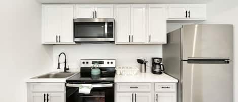A modern kitchen with white cabinets, a stainless steel refrigerator, a microwave, an oven, and a coffee maker.