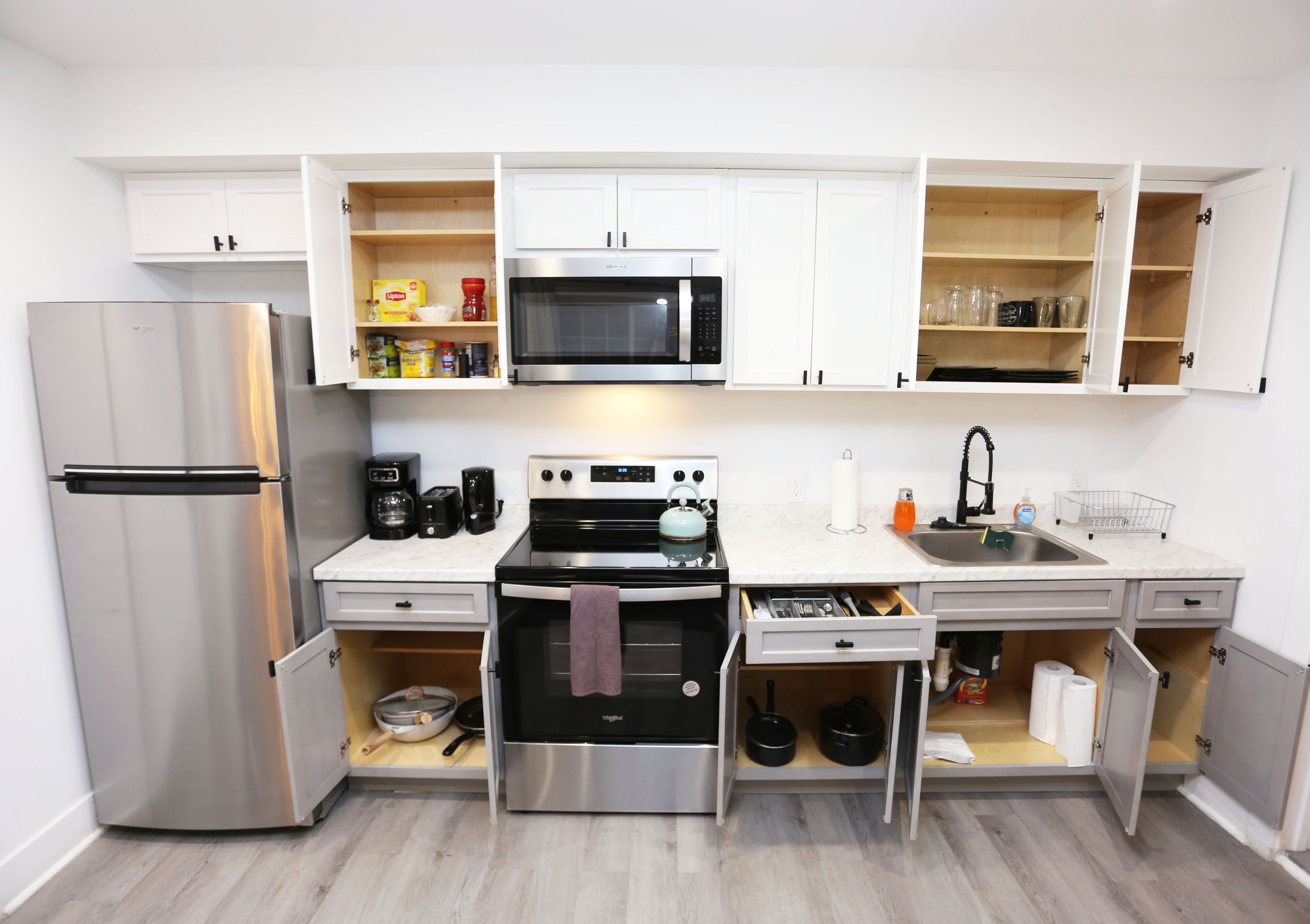 A compact kitchen with a stainless steel refrigerator, a microwave, a stove, and a sink.
