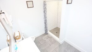 A bathroom with a shower, white walls, and a tiled floor. - Petworth Luxury Unit with Modern Comforts (Washington)