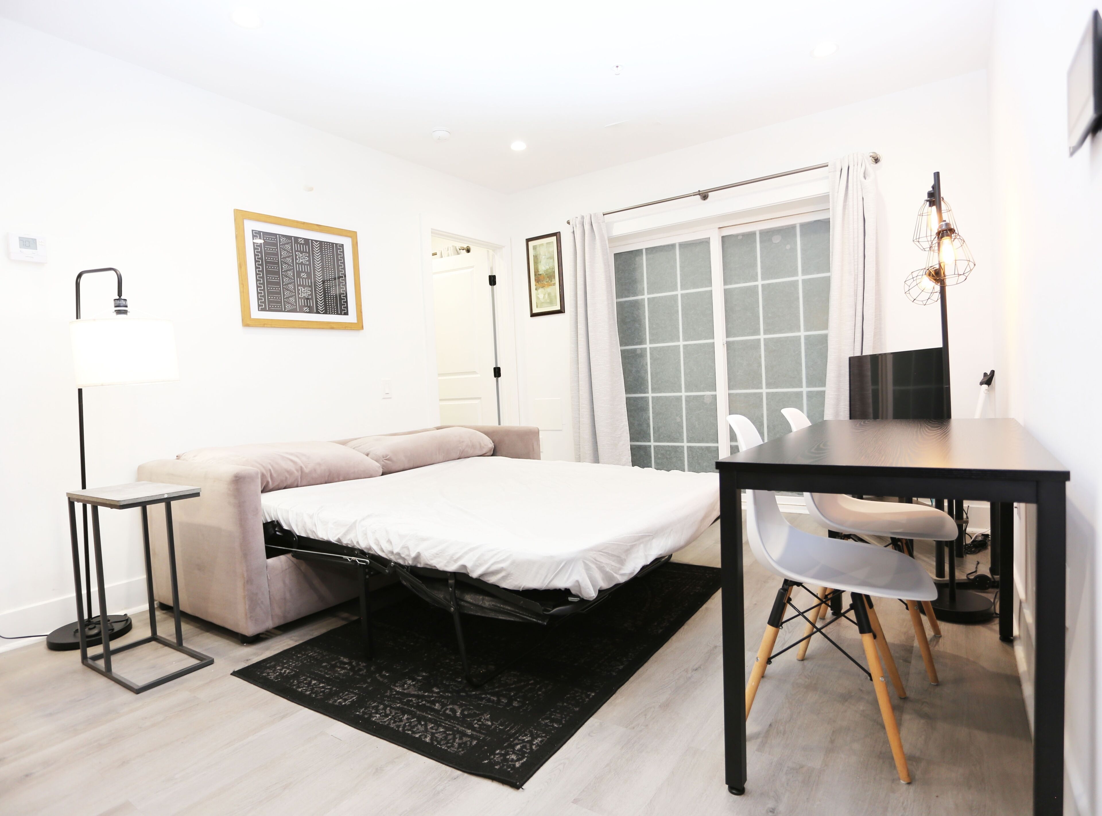 Une chambre moderne avec un lit, un bureau et une chaise. Il y a une fenêtre avec des rideaux, une lampe sur pied et un tableau au mur.